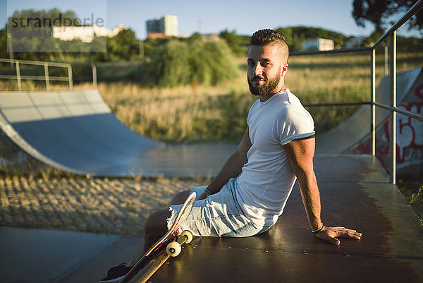 Lächelnder Skateboarder sitzt in einem Skatepark