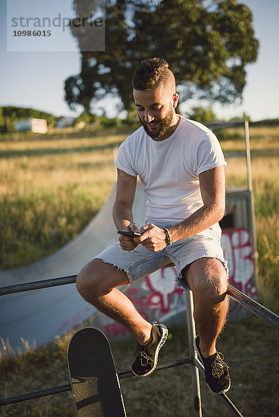 Skateboarder sitzt in einem Skatepark mit dem Smartphone