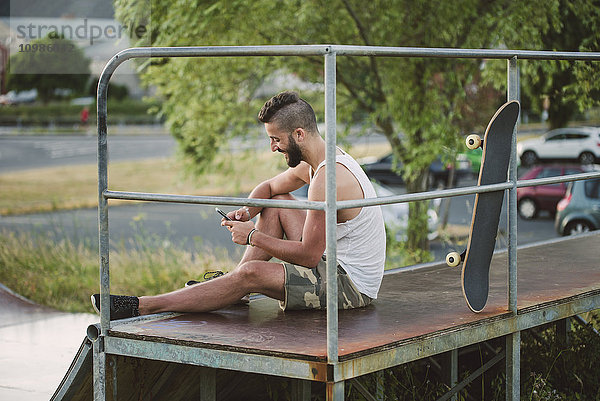 Lächelnder Skateboarder mit seinem Smartphone im Skatepark