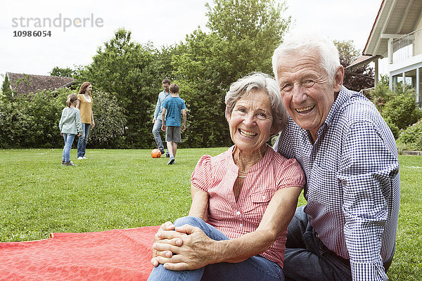 Porträt eines glücklichen Seniorenpaares mit Familie im Hintergrund im Garten