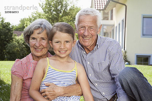 Porträt glücklicher Großeltern mit Enkelin im Garten