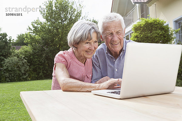 Lächelndes Seniorenpaar mit Laptop im Garten
