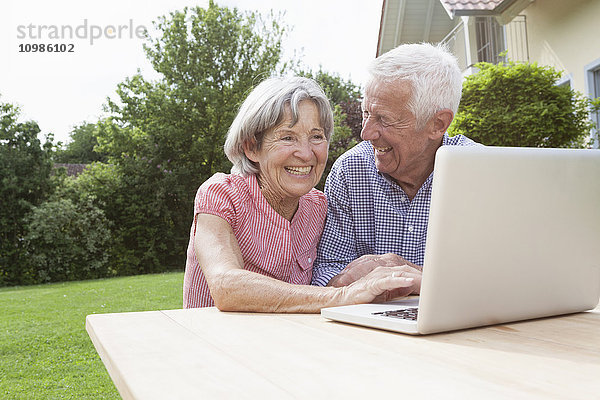 Glückliches Seniorenpaar mit Laptop im Garten