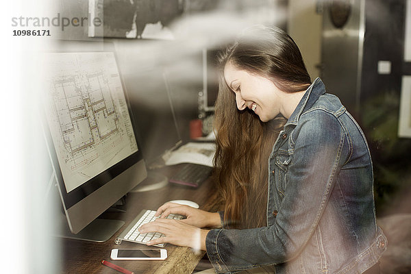 Lachende junge Frau arbeitet am Bauplan am Computerbildschirm