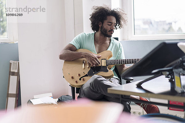 Junger Mann spielt Gitarre im Büro