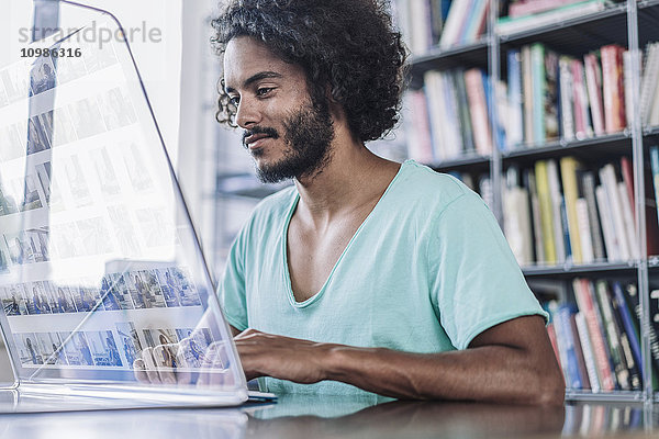 Junger Mann  der in der Bibliothek arbeitet  mit einem futuristischen Computer.