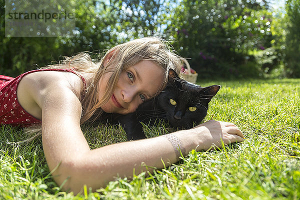 Lächelndes kleines Mädchen auf der Wiese liegend mit schwarzer Katze