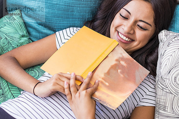 Porträt eines lachenden Teenagermädchens auf der Couch liegend mit Buch