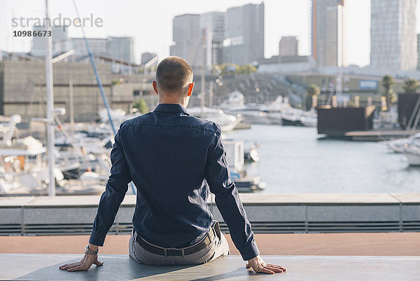 Spanien  Barcelona  Rückansicht eines Geschäftsmannes auf einer Bank mit Blick auf den Hafen