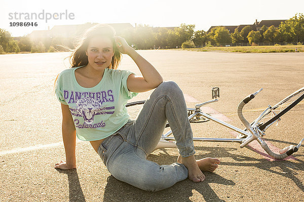 Lächelnde junge Frau mit Fahrrad im Gegenlicht sitzend