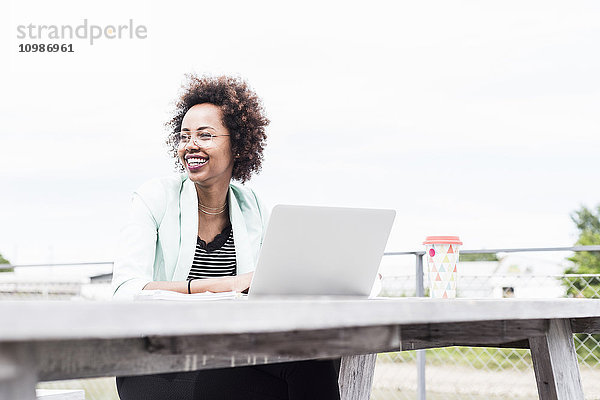 Lächelnde Geschäftsfrau  die draußen mit ihrem Laptop arbeitet.
