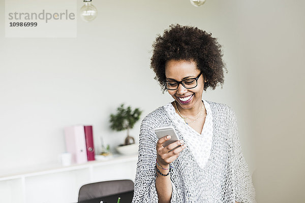 Lächelnde Geschäftsfrau im Büro mit Blick auf ihr Smartphone