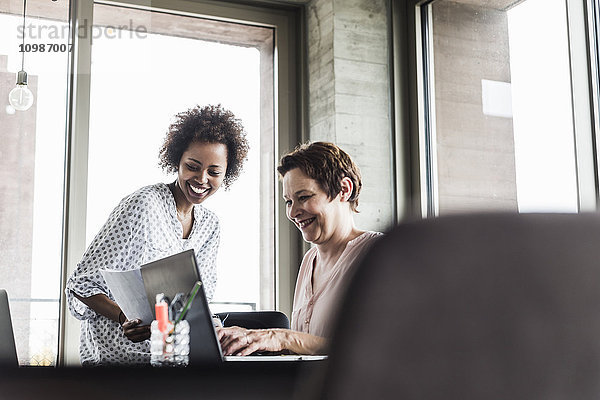 Zwei lächelnde Frauen  die zusammen in einem Büro arbeiten.