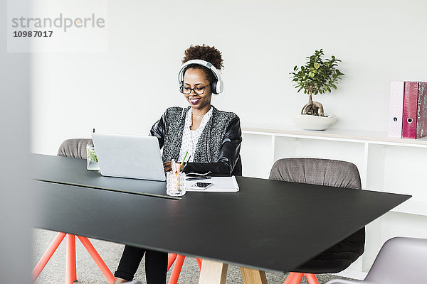Geschäftsfrau mit Kopfhörer am Schreibtisch bei der Arbeit mit Laptop