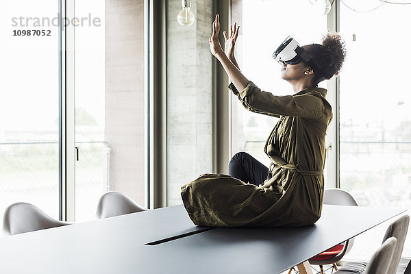 Frau im Büro sitzend auf dem Konferenztisch mit Virtual-Reality-Brille