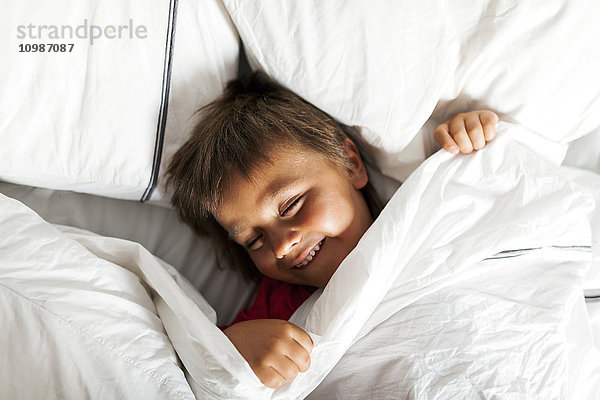 Lächelnder kleiner Junge  der im Bett liegt und versucht zu schlafen.