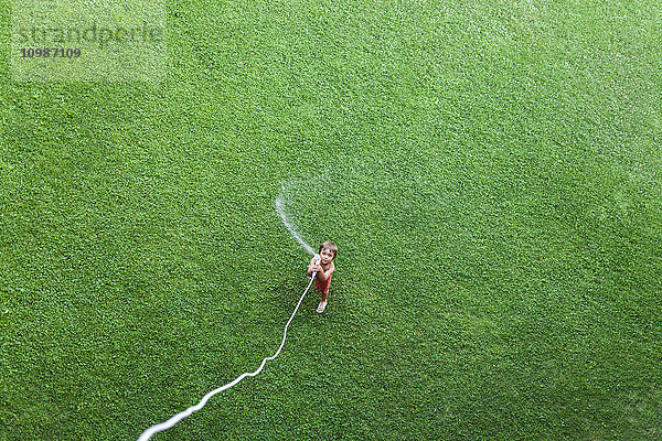 Kleiner Junge auf dem Rasen stehend mit Gartenschlauch  Draufsicht