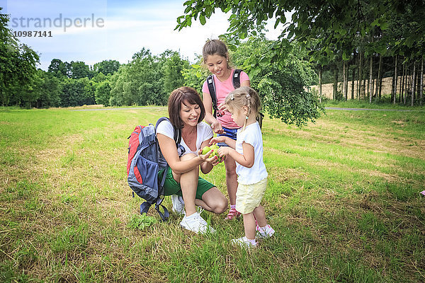 Mutter schenkt Äpfel  Mutter und Töchter auf der Wiese beim Wandern