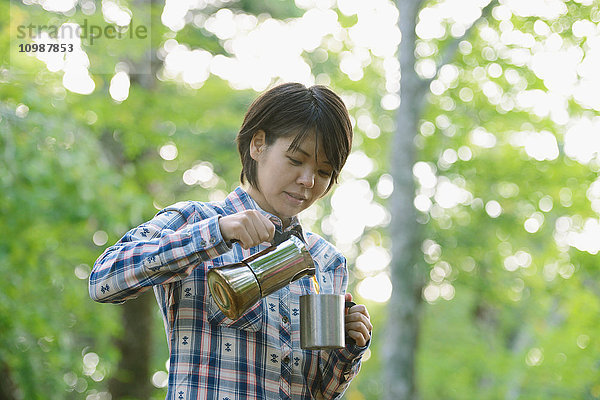 Junge Japanerin beim Kaffeetrinken auf einem Campingplatz
