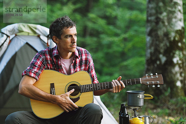 Kaukasischer Mann spielt Gitarre auf einem Campingplatz