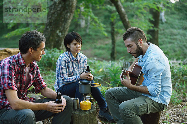 Multiethnische Gruppe von Freunden spielt Gitarre auf einem Campingplatz