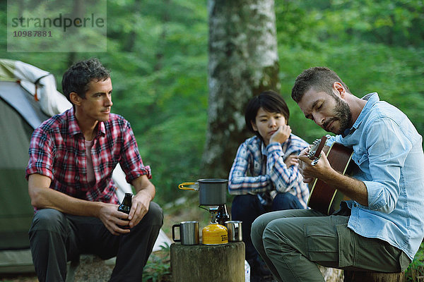 Multiethnische Gruppe von Freunden spielt Gitarre auf einem Campingplatz