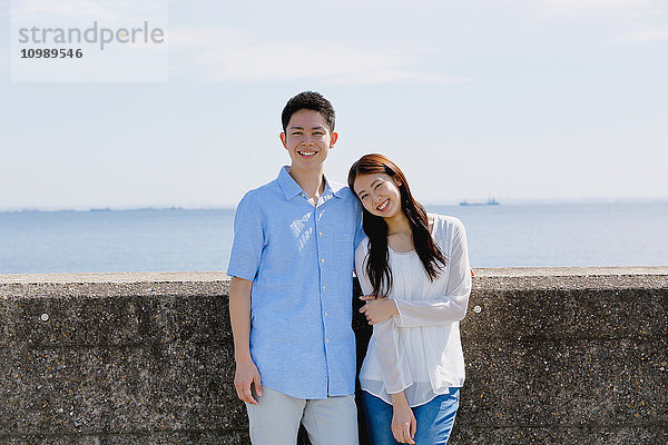 Junges japanisches Paar lehnt an einer Betonmauer am Meer