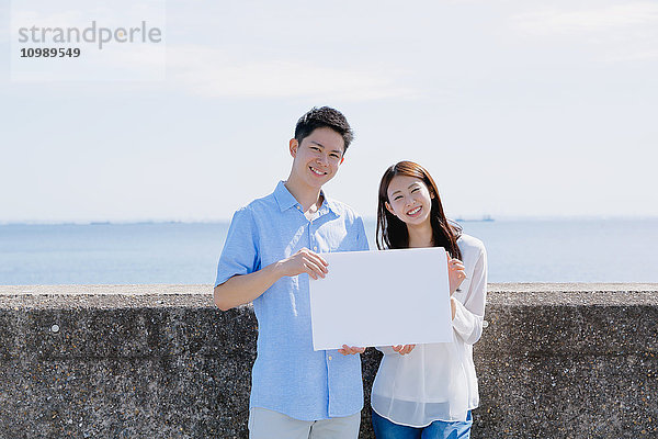 Junges japanisches Paar mit Whiteboard am Meer