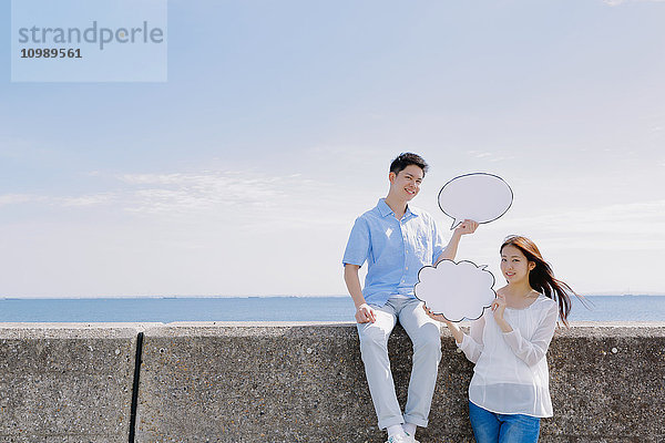Junges japanisches Paar mit Anzeigetafeln am Meer