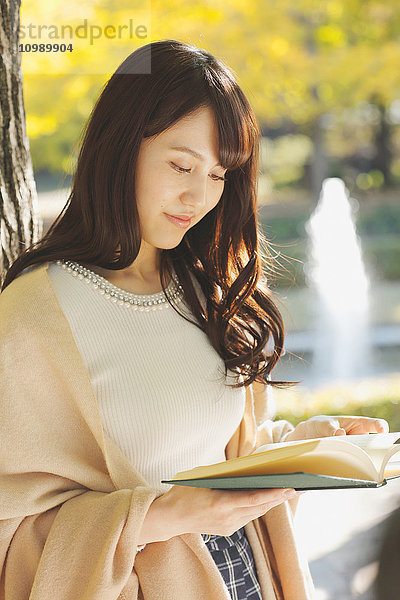 Junge Japanerin mit Buch in einem Stadtpark