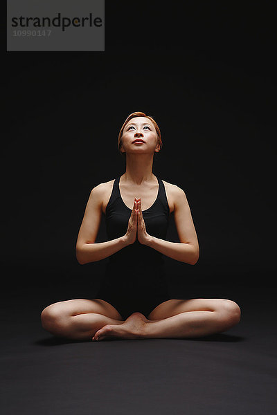 Attraktive junge Japanerin in schwarzer Hose und Tanktop übt Yoga auf schwarzem Hintergrund