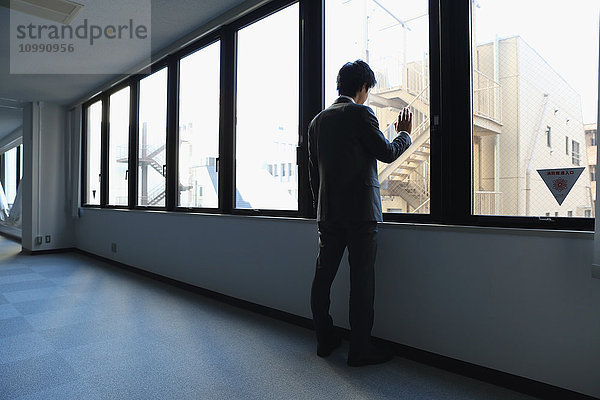 Japanischer Geschäftsmann schaut in einem leeren Büro aus dem Fenster