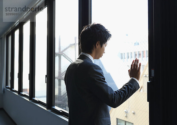 Japanischer Geschäftsmann schaut in einem leeren Büro aus dem Fenster