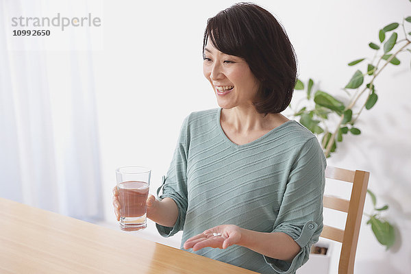 Ältere Japanerin nimmt Pillen im Wohnzimmer
