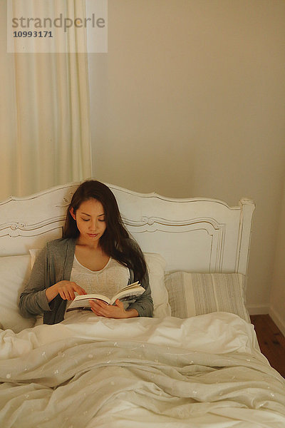 Junge attraktive japanische Frau liest im Bett