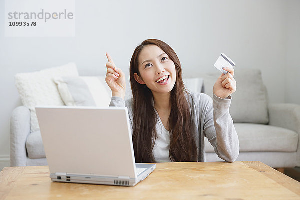 Junge attraktive japanische Frau beim Online-Shopping zu Hause