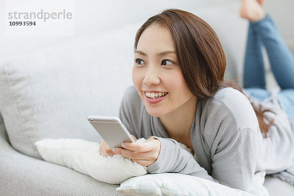 Junge attraktive japanische Frau mit Smartphone auf dem Sofa