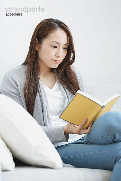 Junge attraktive Japanerin mit Buch auf dem Sofa