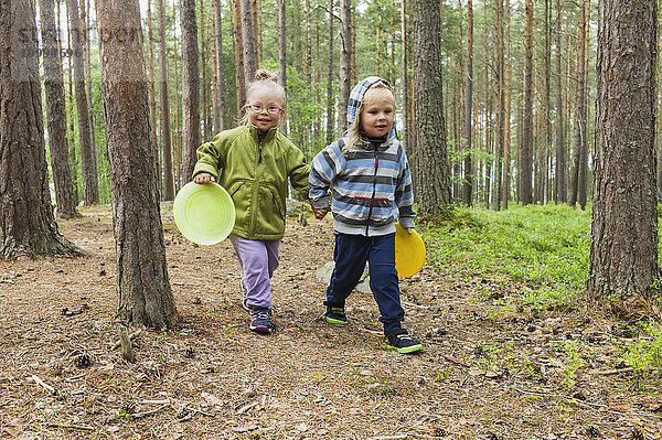 4 Jahre alte Geschwister  die mit ihren Frisbees durch den Wald laufen  Schweden