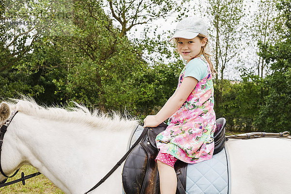 5 Jahre altes Mädchen schaut in die Kamera beim Reiten auf einem weißen Pferd  Deutschland