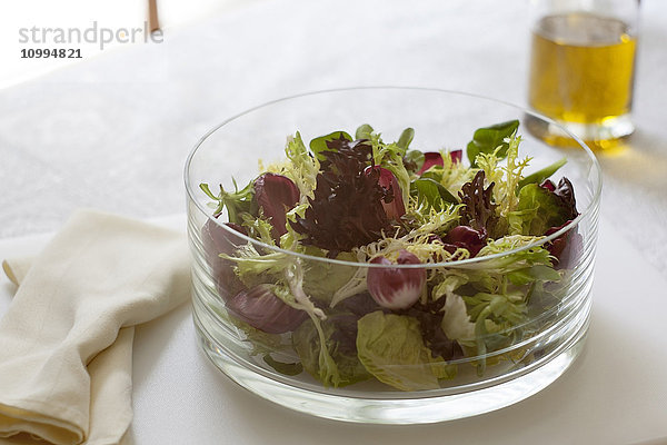 Nahaufnahme von Salat in einer Glasschüssel mit Serviette und einer Flasche Olivenöl