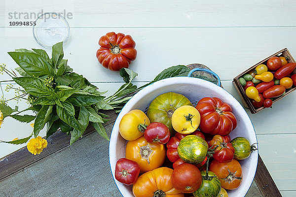 Draufsicht auf eine Schüssel mit Tomaten und ein Bündel frisches Basilikum auf dem Tisch