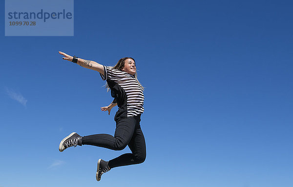 Junge Frau springt gegen den klaren Himmel