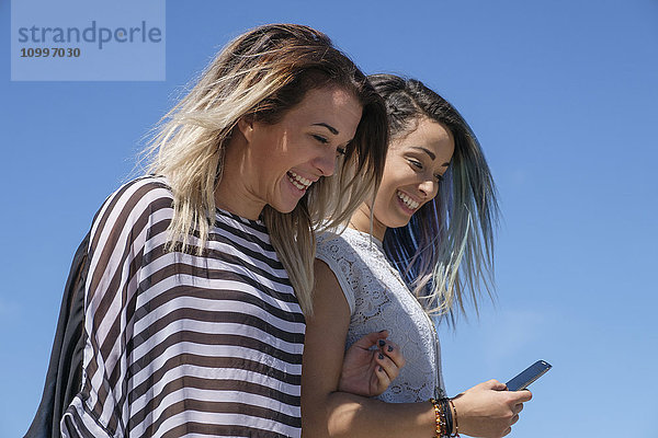 Junge Frauen lachen und schauen auf ihr Mobiltelefon