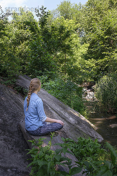 Frau sitzt auf einem Stein im Wald