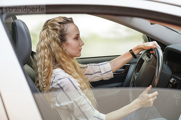Frau mit lockigem  langem  blondem Haar fährt Auto