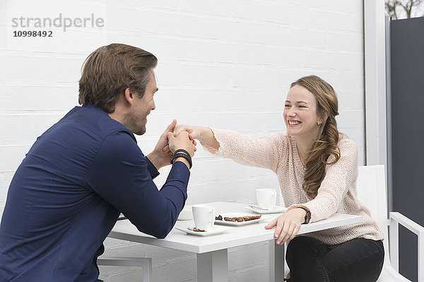 Mann hält die Hand einer Frau  während sie am Tisch sitzen und Kaffee trinken