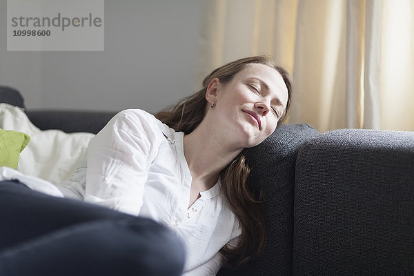 Mittlere erwachsene Frau auf dem Sofa liegend  mit geschlossenen Augen und lächelnd