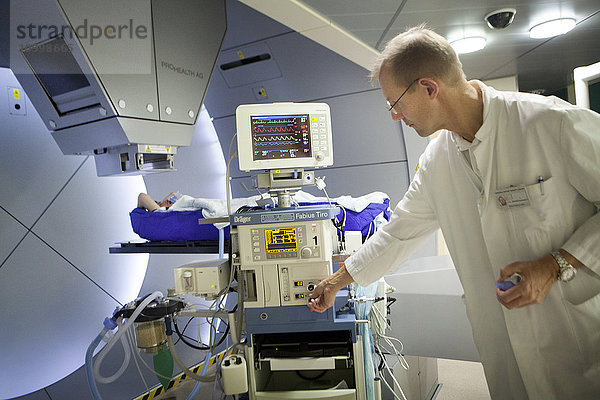 Reportage über das Rinecker Protonentherapiezentrum in München  Deutschland. Das Zentrum verfügt über die modernste Ausrüstung für die Protonentherapie-Behandlung. Bei der Protonentherapie werden Krebszellen bestrahlt  indem ein Protonenstrahl auf den Kern des Tumors konzentriert wird  während das gesunde umliegende Gewebe geschont wird. Die Einstellungen der Software ermöglichen eine präzise Ausrichtung des Tumors. Zur Behandlung von Tumoren an Organen  die sich während der Atmung bewegen  wird der Patient in künstliche Apnoe versetzt.