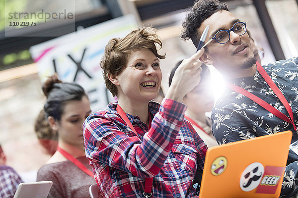 Lächelnde Frau mit Laptop zeigt auf Technologiekonferenz